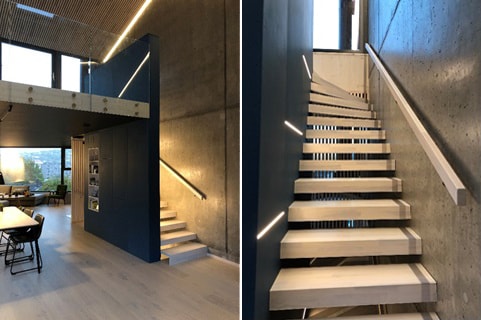 Moderne trapp med integrert LED-lys i håndløperen og lamper i vangen, med betongvegg og lyse eiketrinn.