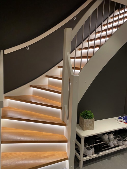 Svingt trapp med LED-strips under utstikket på hvert trinn, som gir et jevnt lys på trinnene.