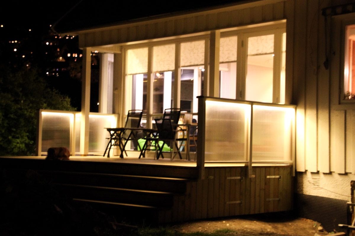 Terrasse med skjermvegger av matte plater som er lyst opp med LED-lys en mørk kveld.